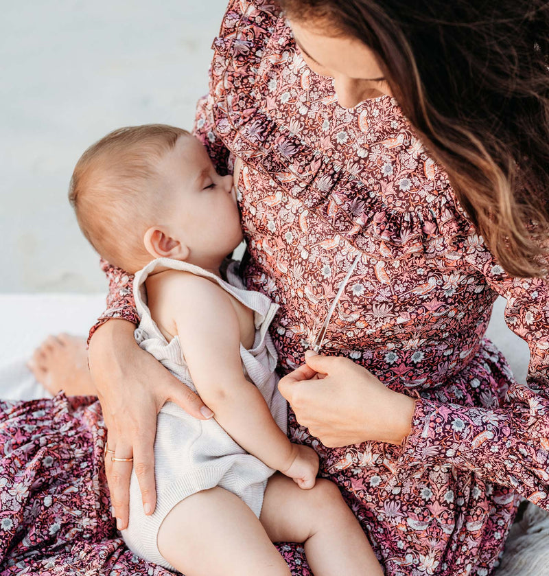 Women sitting breastfeeding her baby wearing the Ellie and Becca Nursing Dress Belle made of organic Liberty Fabric featuring two hidden zippers convienent for breastfeeding.
